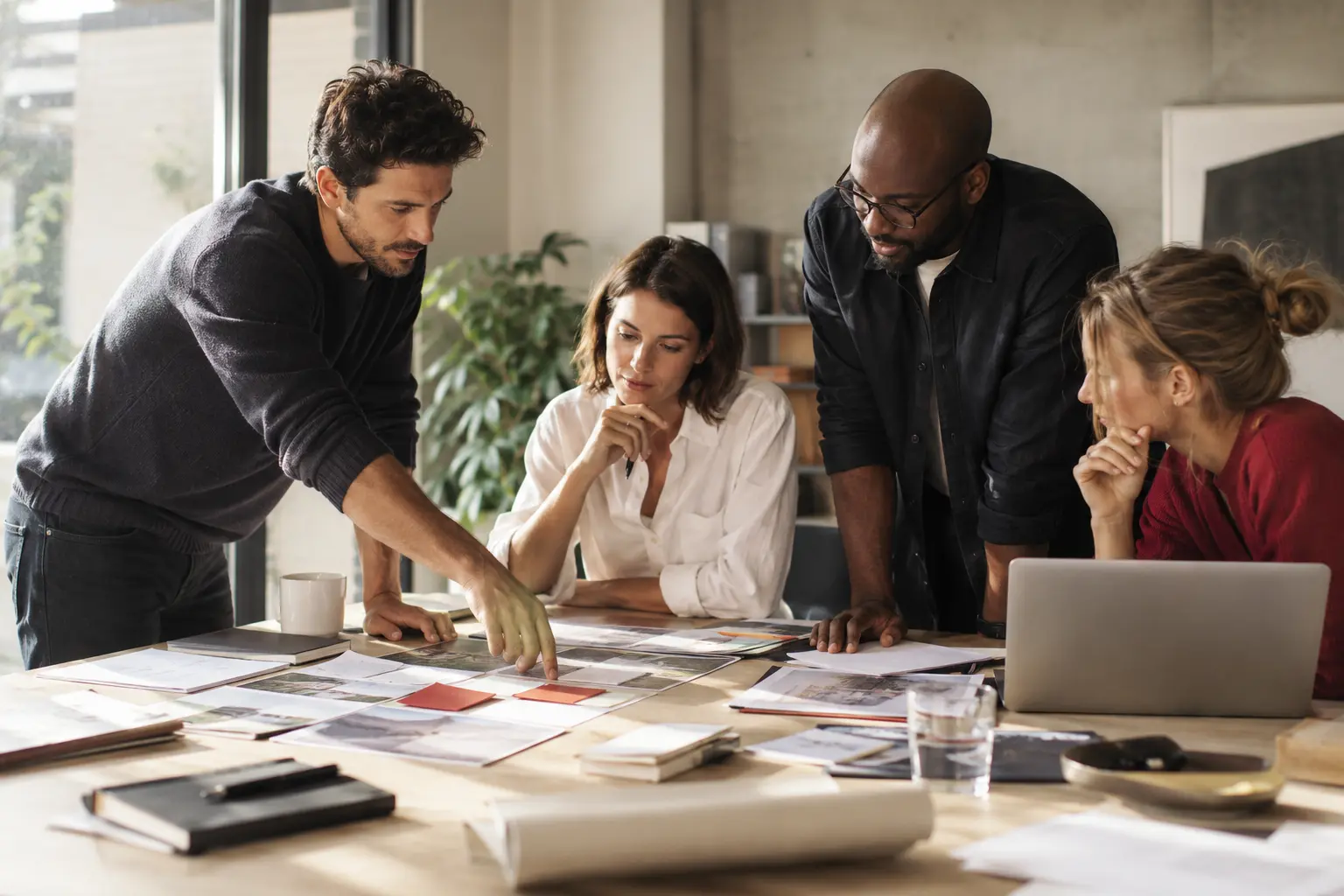 A business project planning session with paper workflow cards, documents and a laptop laid out neatly on a large table, realistic tactile materials.