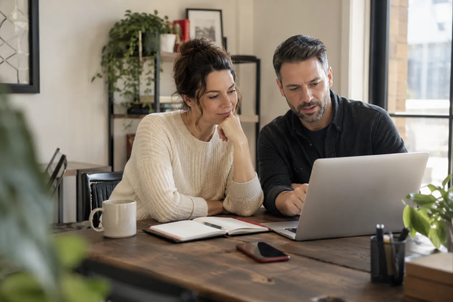 A local business owner reviewing a clean website prototype on a laptop with a consultant, a phone and appointment notebook nearby.