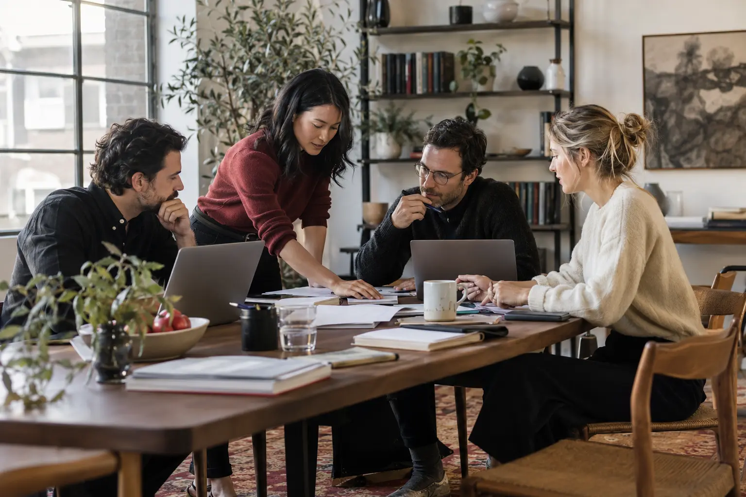 An independent business team reviewing their day-to-day operations around a shared worktable, laptops and ordinary business paperwork, calm and capable.